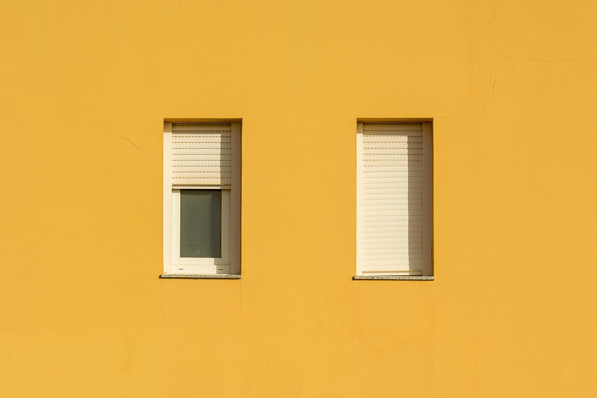 Two windows with roller shutters on a yellow building.