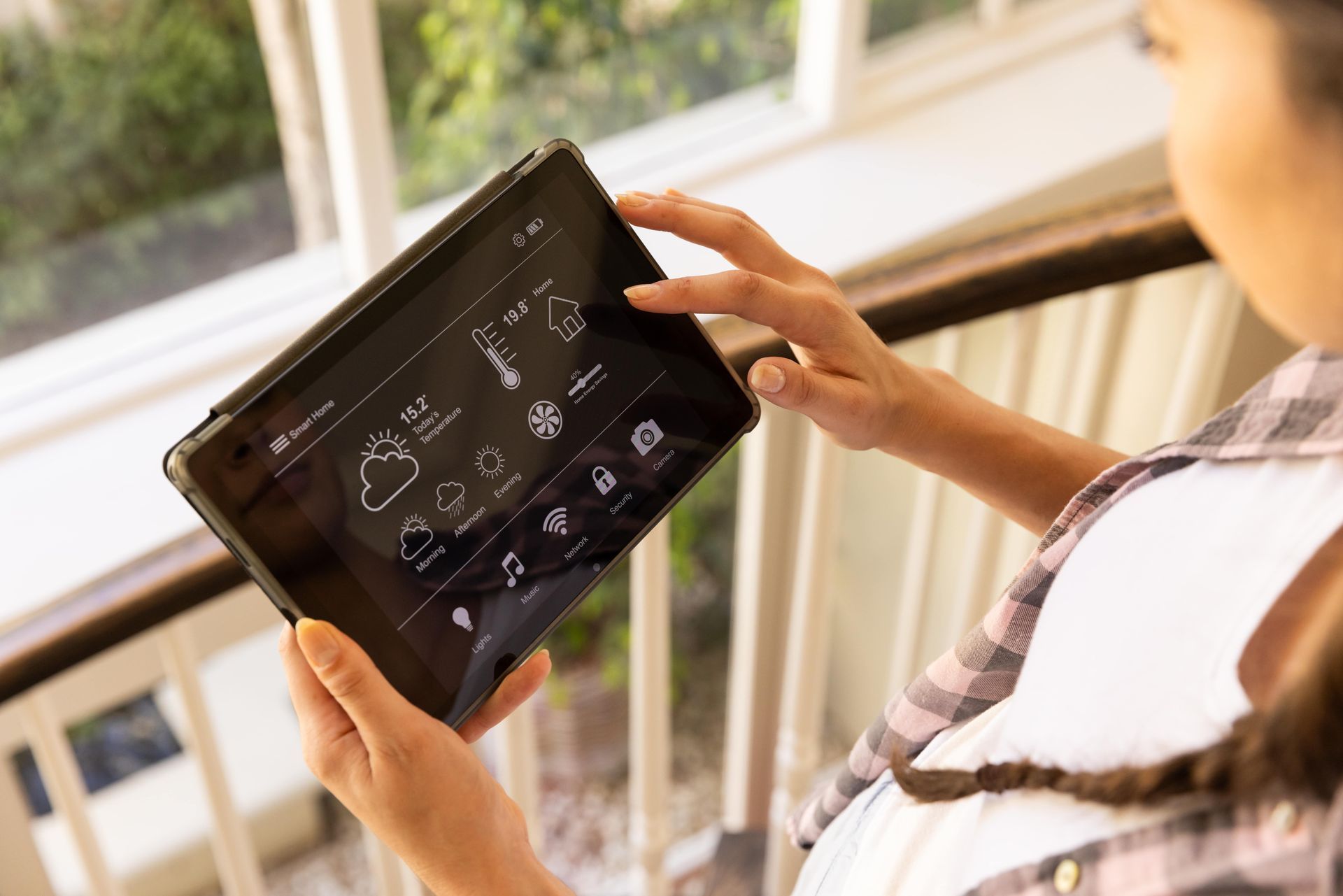 A woman is holding a tablet in her hands in front of a window.