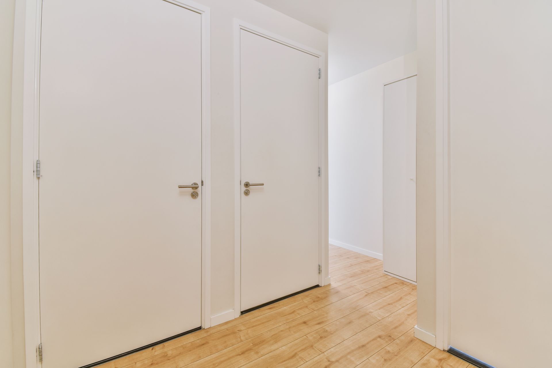 A hallway with white doors and wooden floors in a house.