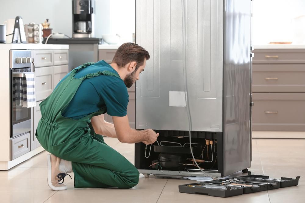 A Male Technician Repairing A Refrigerator At Home — North West Heating, Cooling and Refrigeration in Taminda, NSW