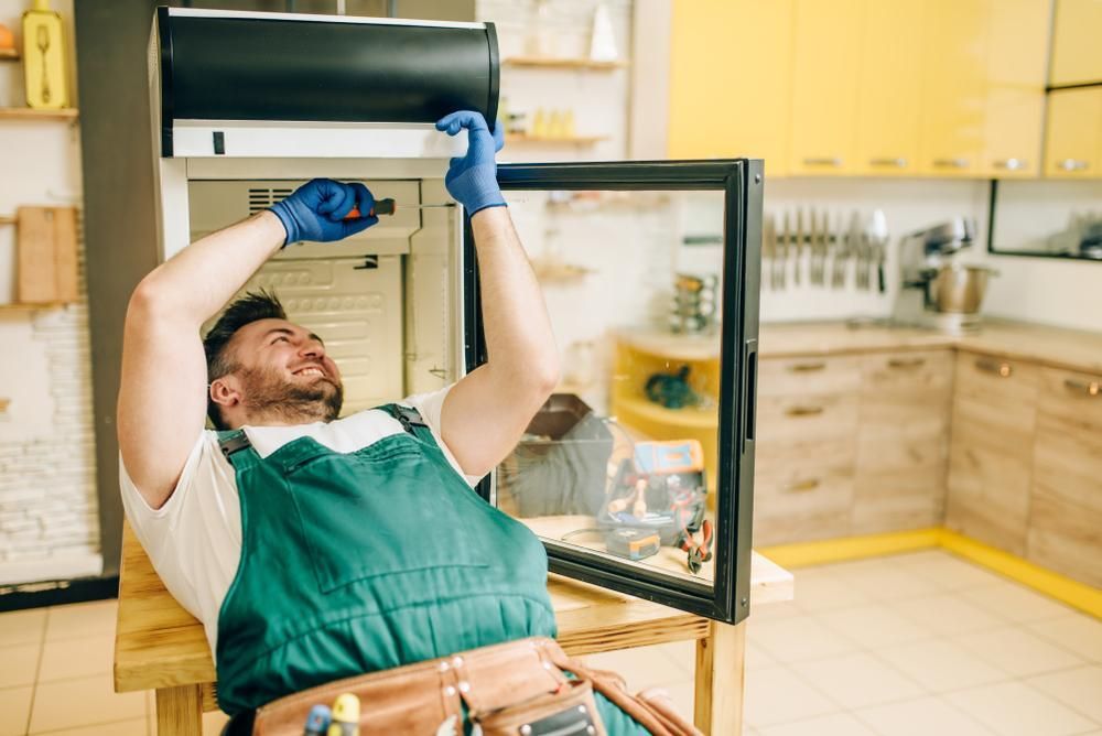 A Worker In Gloves Repairing A Refrigerator At Home — North West Heating, Cooling and Refrigeration in Taminda, NSW