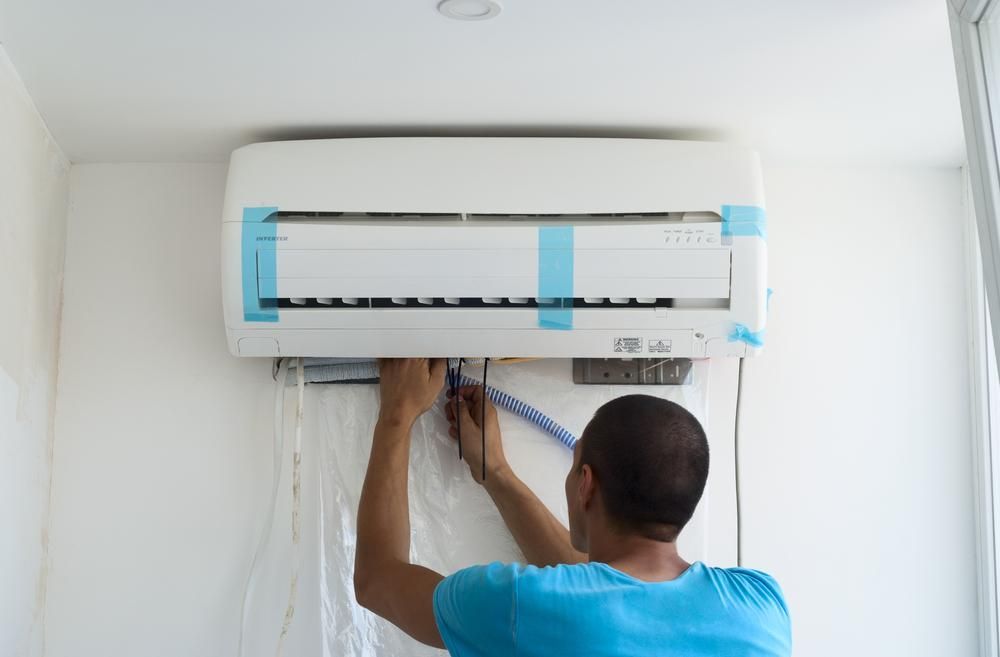 A Man Is Measuring A Wall Mounted Air Conditioner With A Tape Measure — North West Heating, Cooling and Refrigeration in Narrabri, NSW