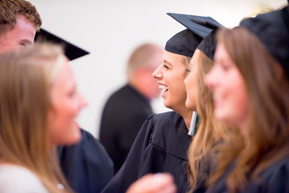 Graduates in caps and gowns chatting and smiling at a commencement ceremony