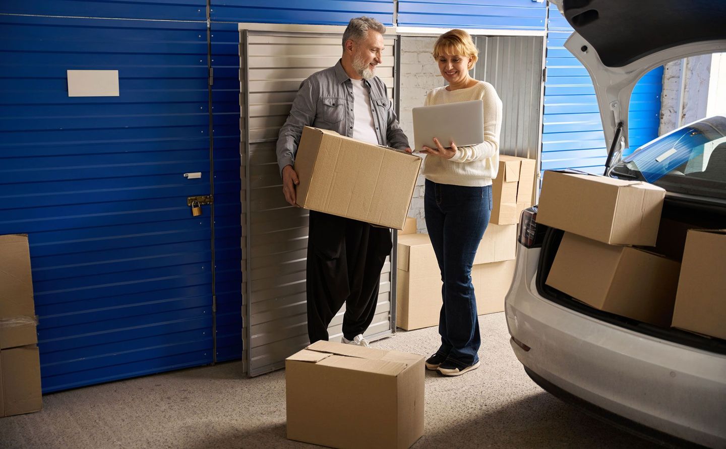 A man and a woman are loading boxes into a car in a garage.