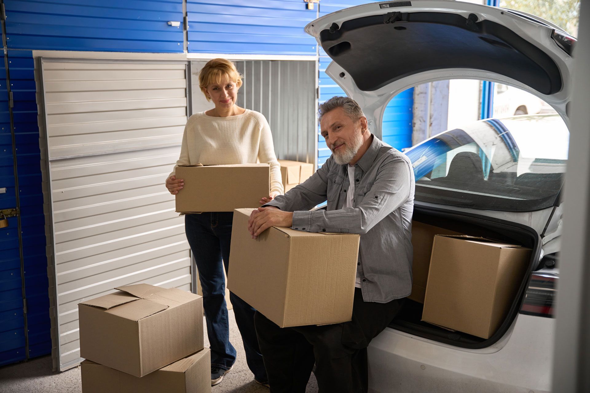 A man and a woman are loading boxes into the back of a car.