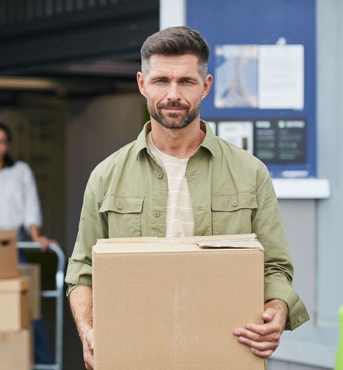 A man in a green shirt is holding a cardboard box.