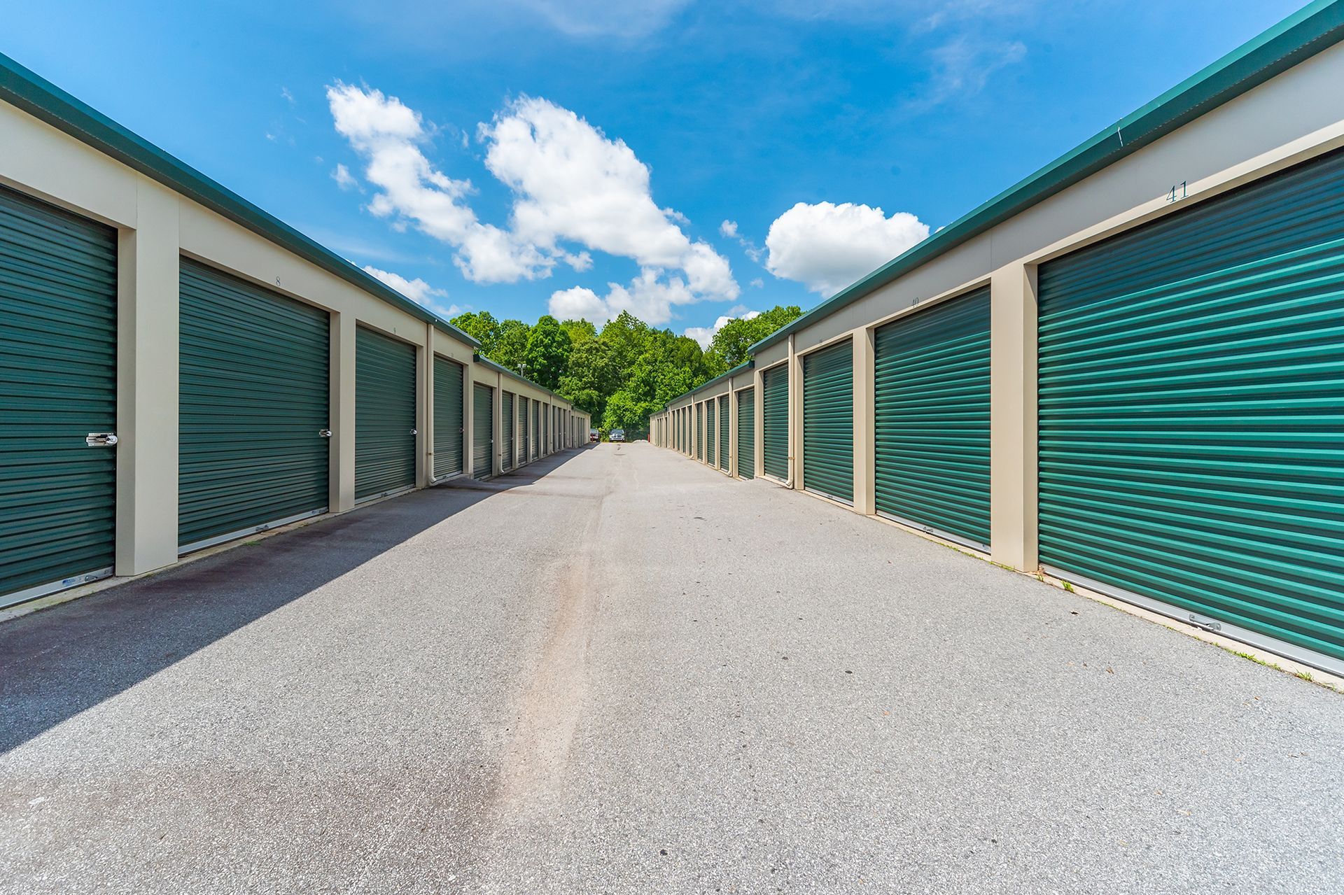 A row of green garage doors are lined up on a gravel road.