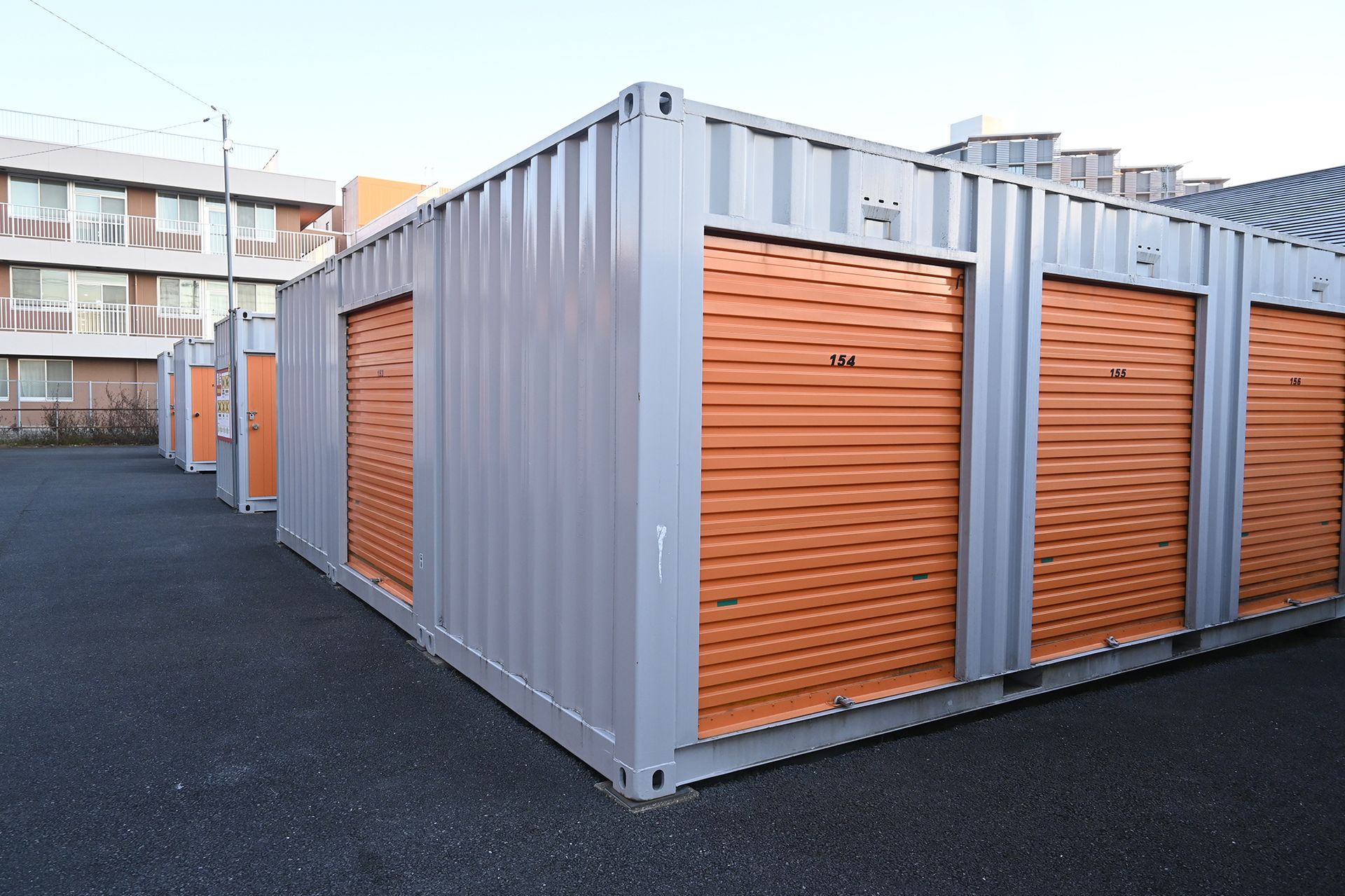 A row of storage containers with orange doors in a parking lot.