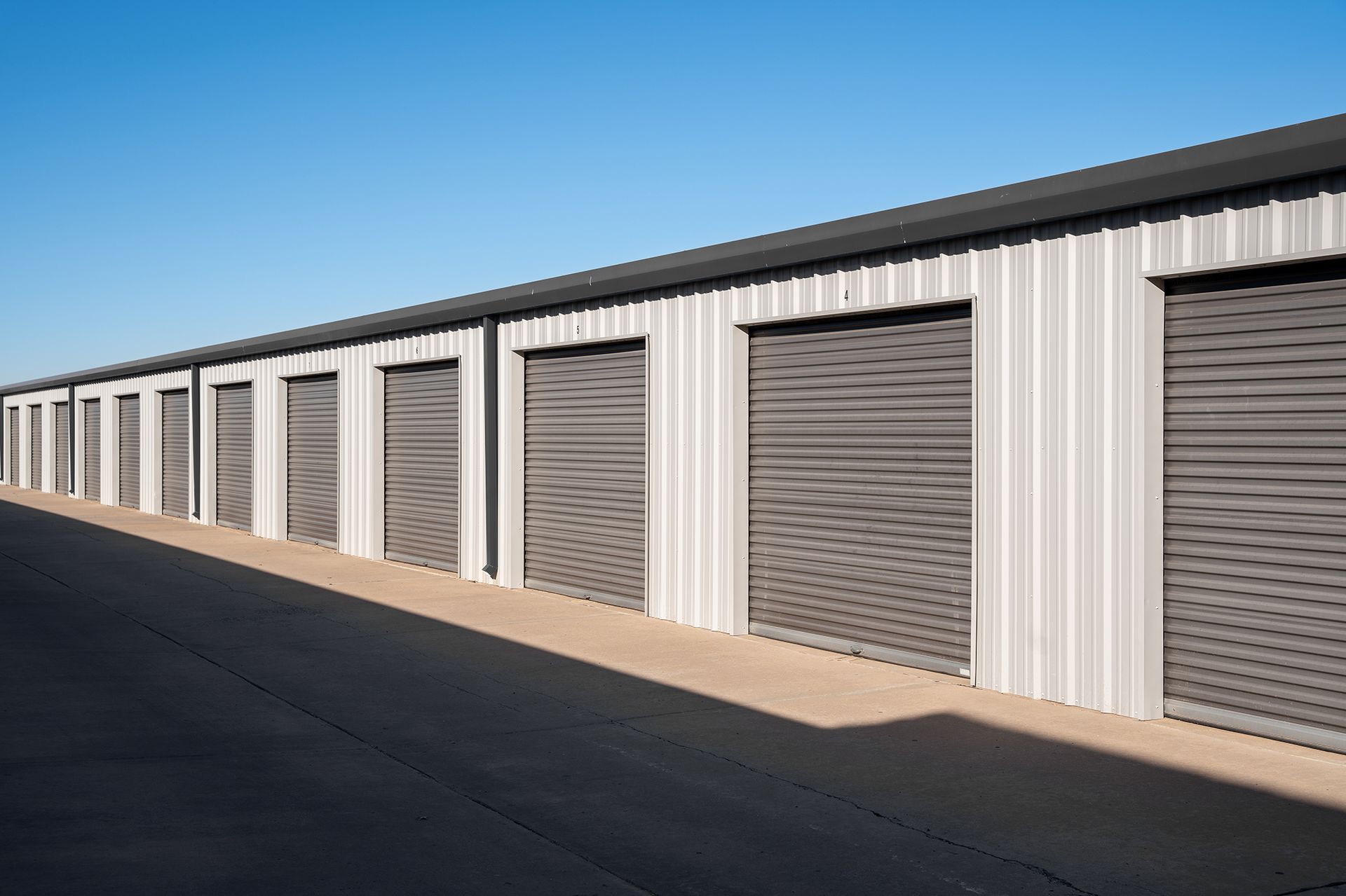 A row of storage units with roller doors on a sunny day.