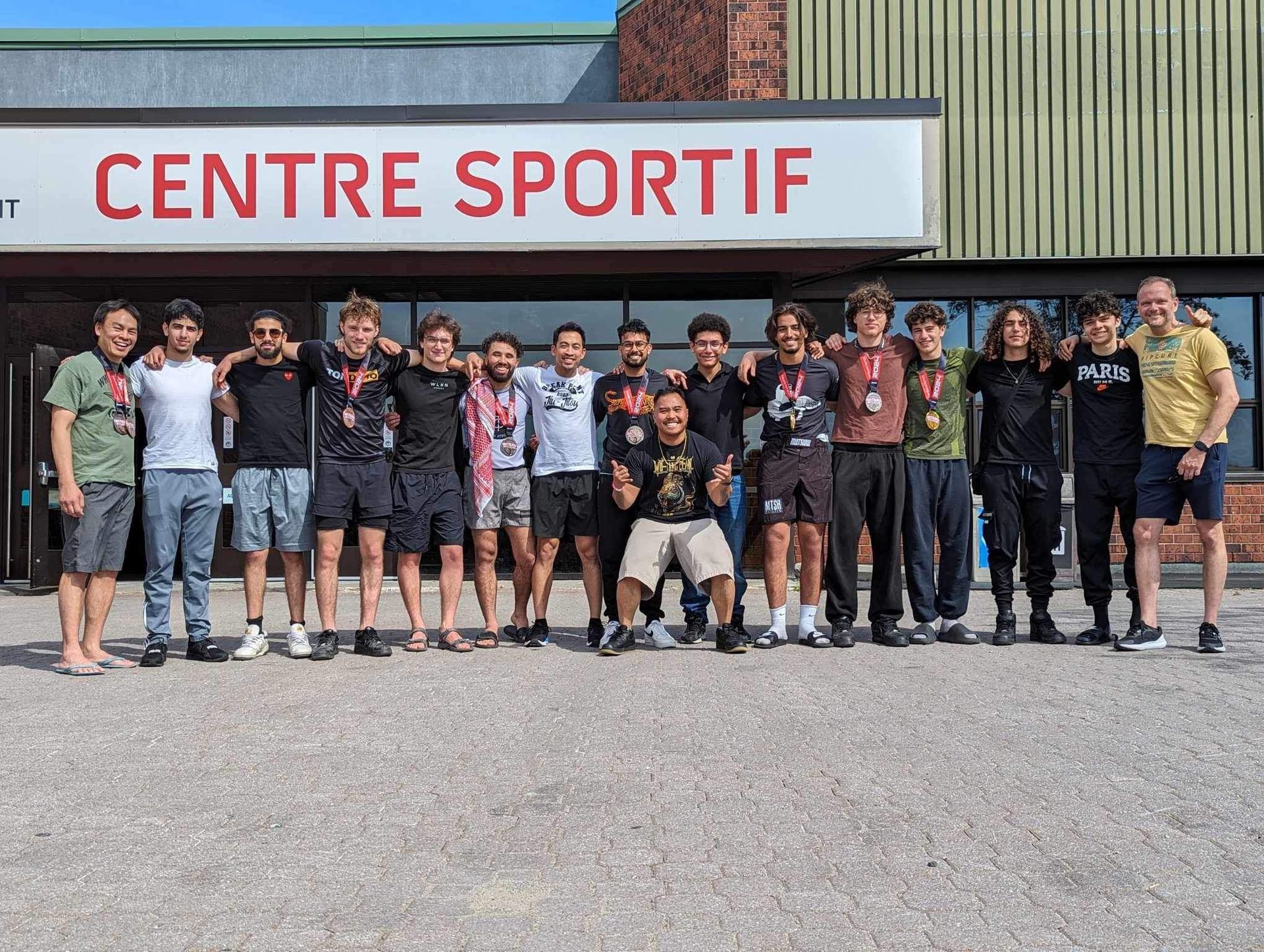 Groupe de jeunes hommes avec des médailles devant un bâtiment avec l'inscription 