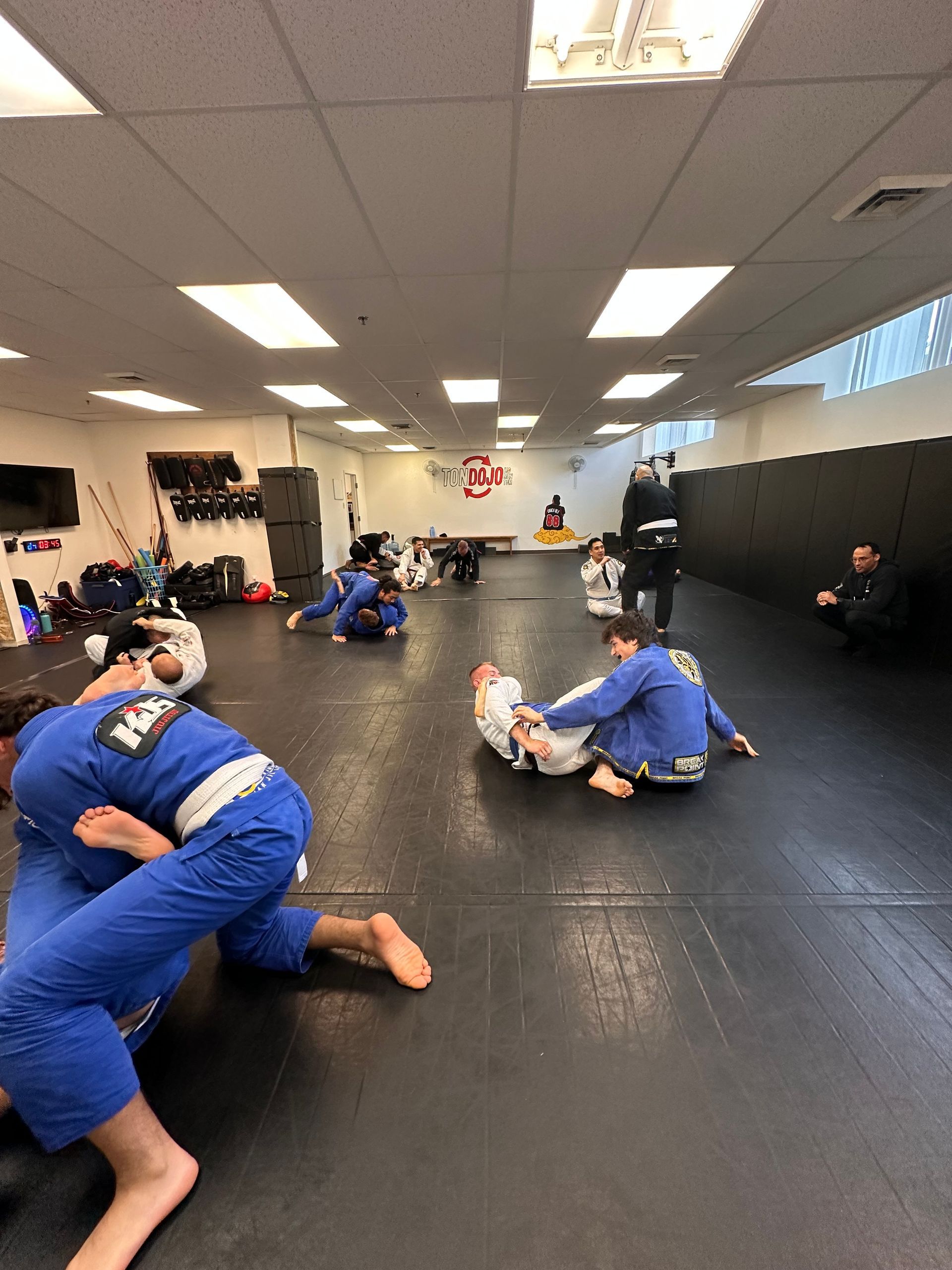 Des gens en kimono bleu pratiquant le Jiu-Jitsu sur des tapis à l'intérieur d'une salle de sport.