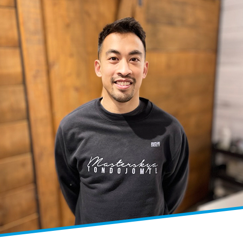 A man wearing a black sweatshirt is standing in front of a wooden wall.