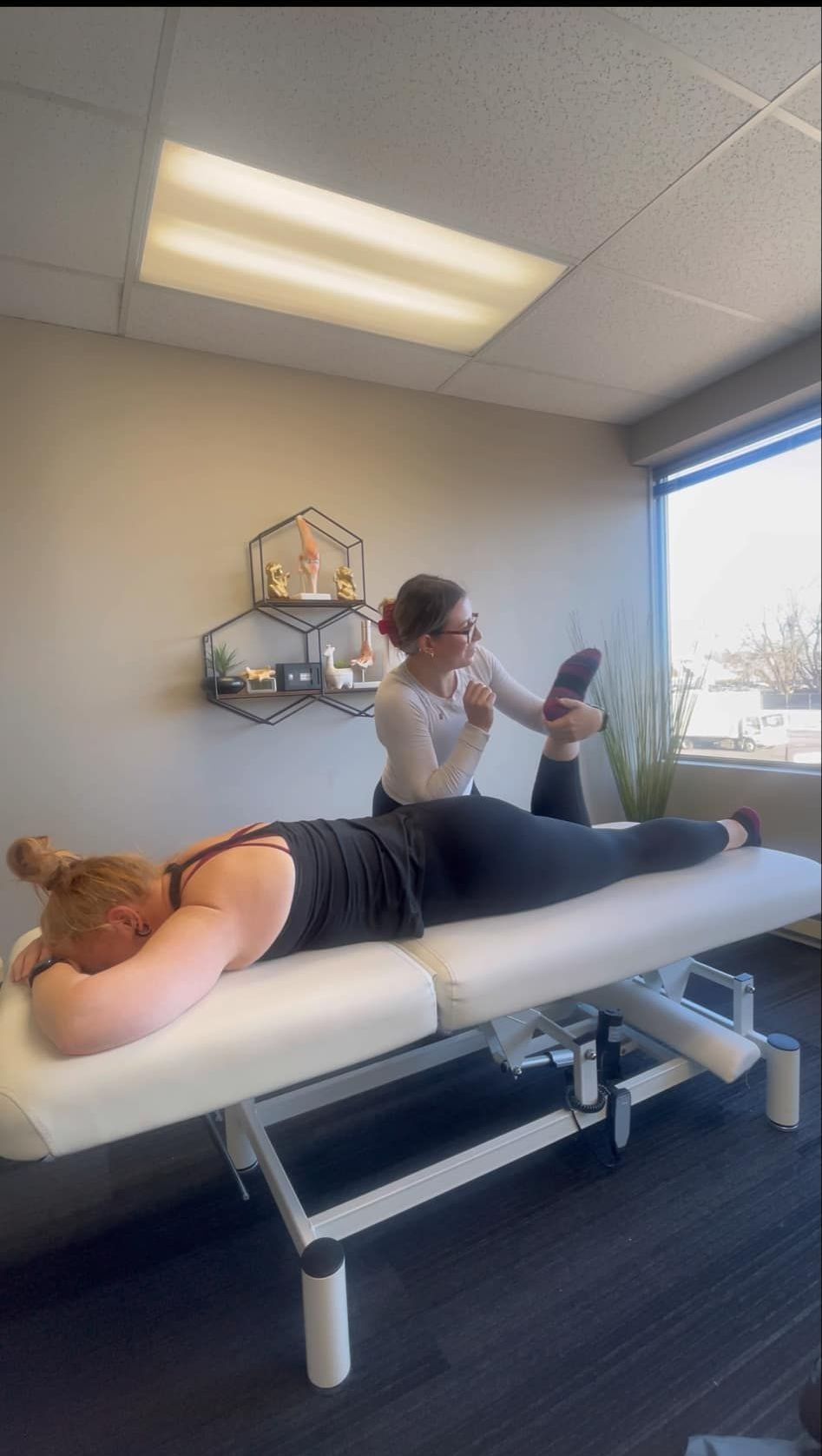 Une femme reçoit une thérapie physique sur une table de massage ; le thérapeute tient un miroir et examine sa jambe.