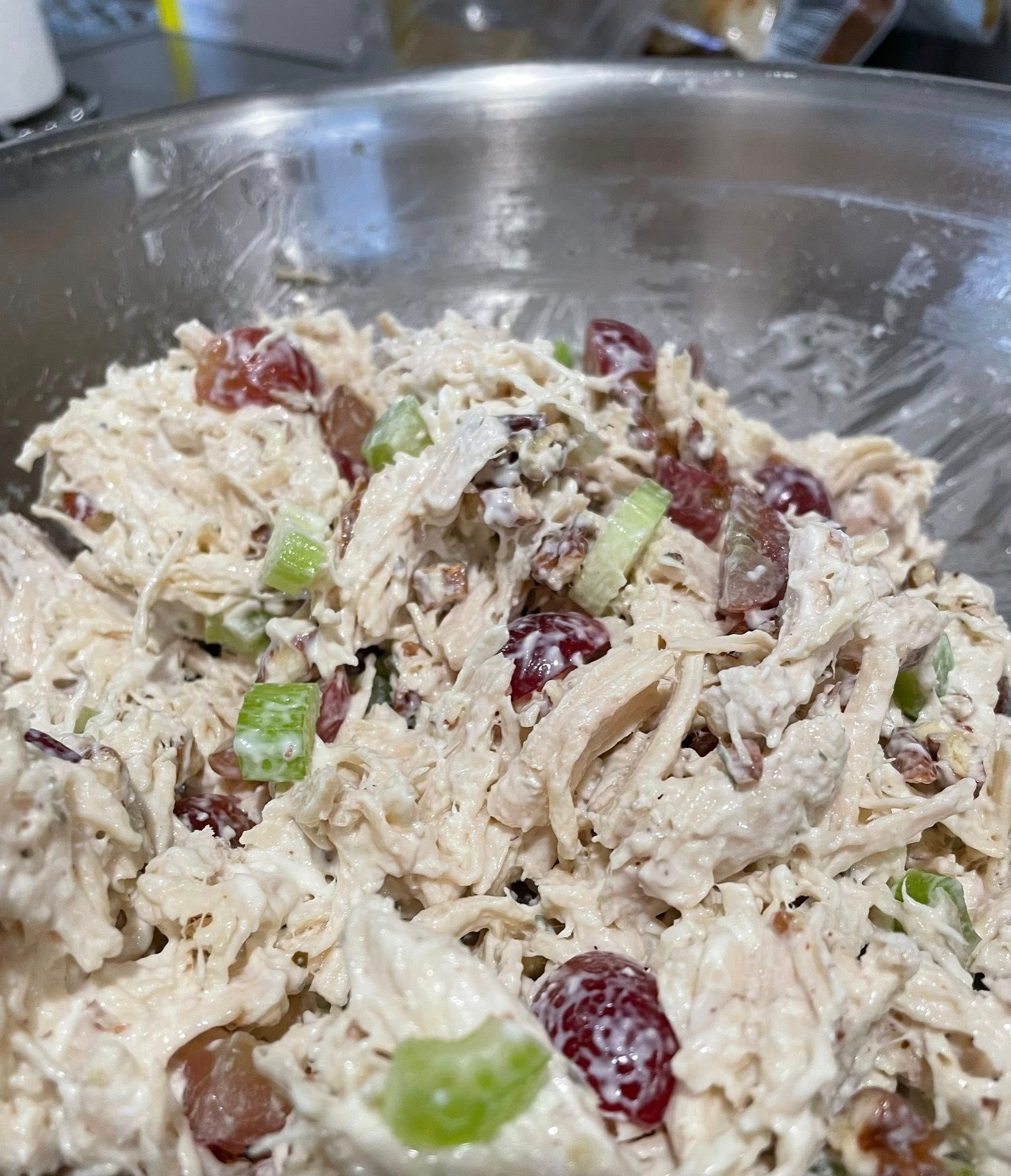 Chicken salad with red grapes and celery in a stainless steel mixing bowl.