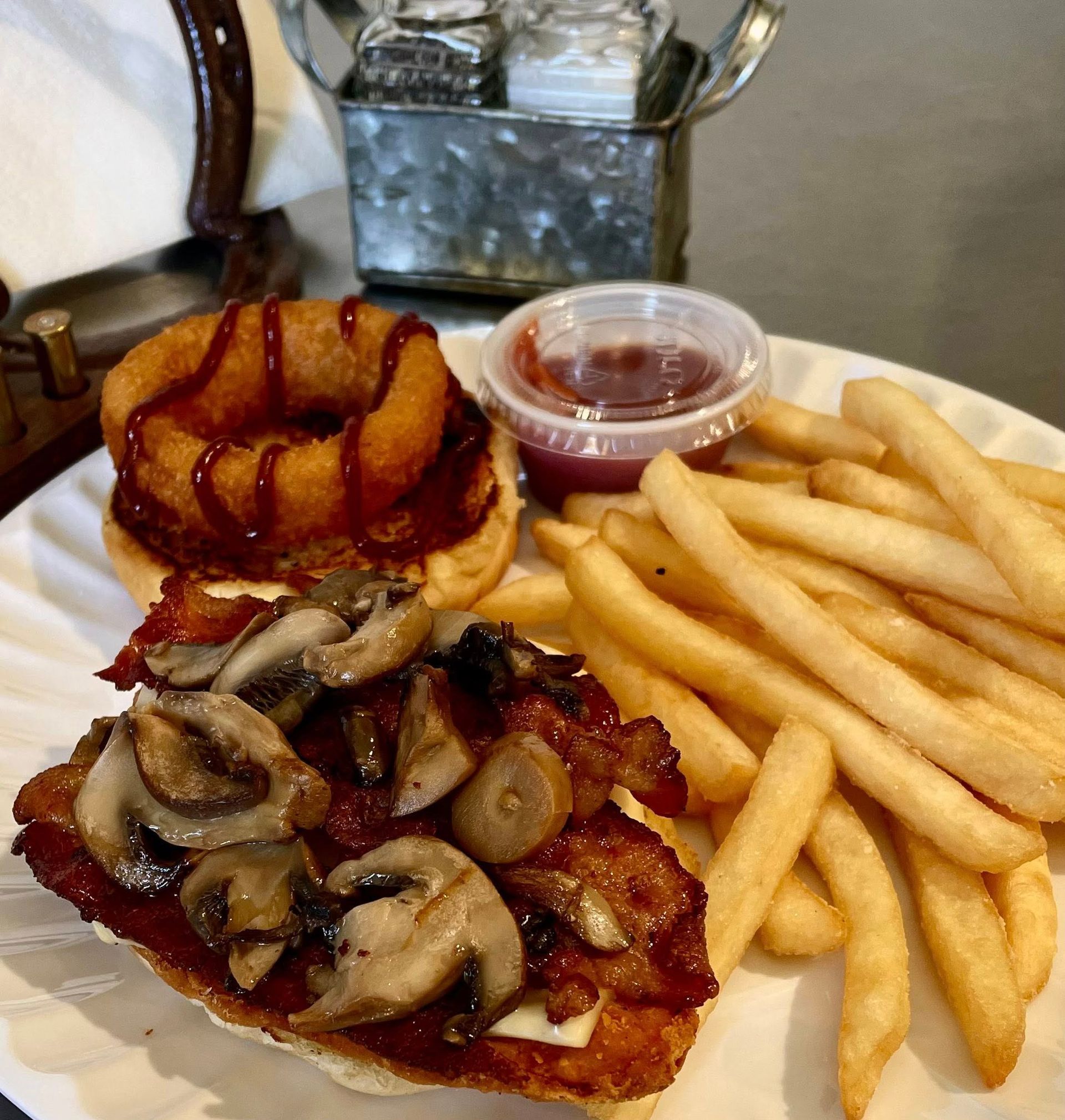 A plate of food: a sandwich topped with mushrooms and onion ring, fries, and ketchup.