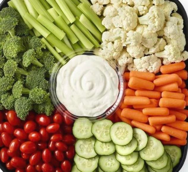 Vegetable platter with broccoli, celery, cauliflower, carrots, cherry tomatoes, and cucumber slices arranged around a central dip.