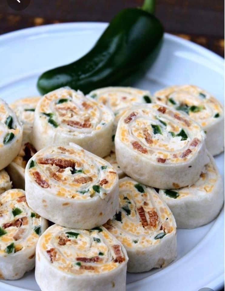 Close-up of tortilla pinwheels filled with cheese, bacon, and jalapeños on a white plate, with a whole jalapeño pepper in the background.