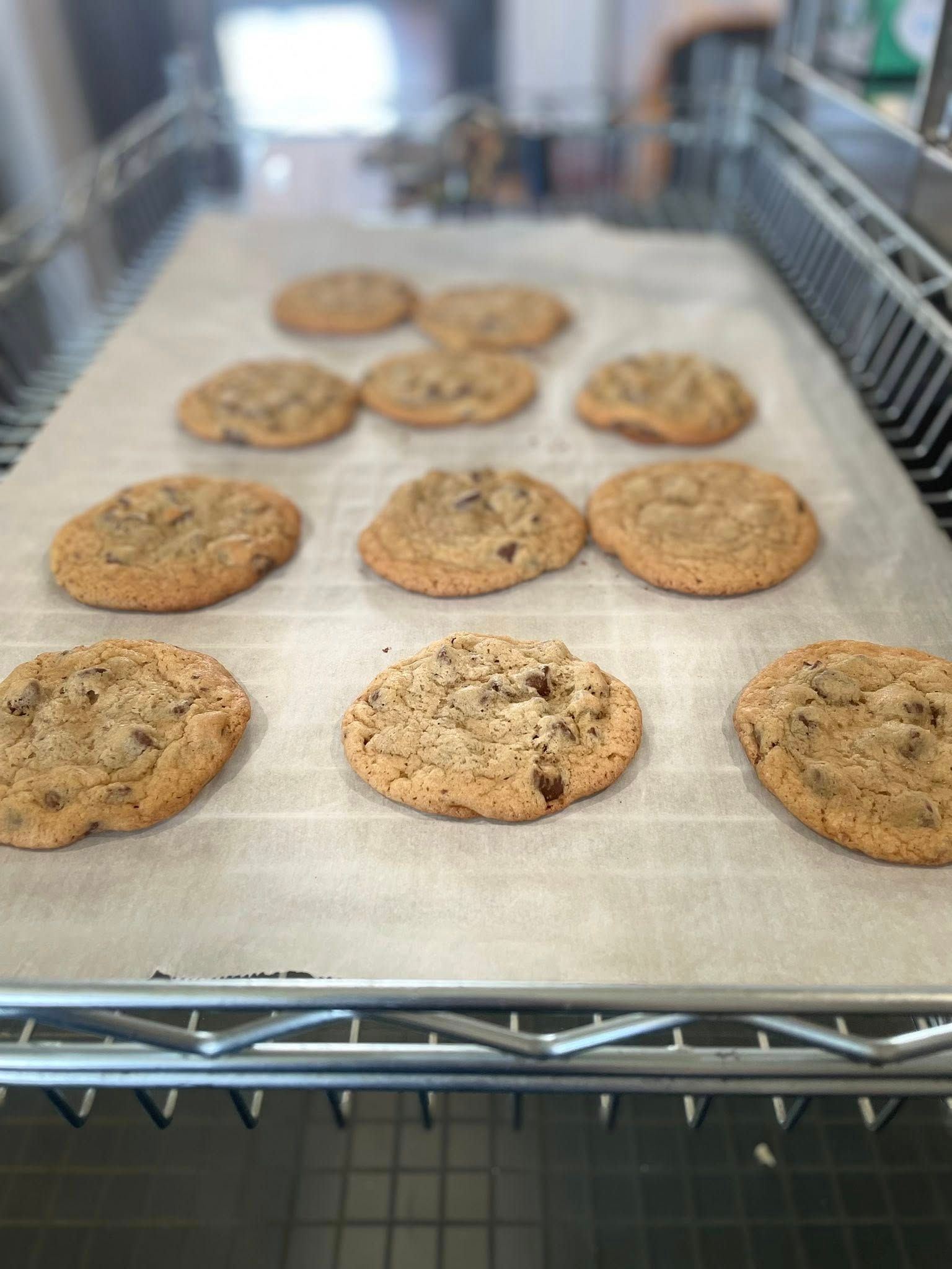 Baked chocolate chip cookies on parchment paper, cooling on a wire rack.