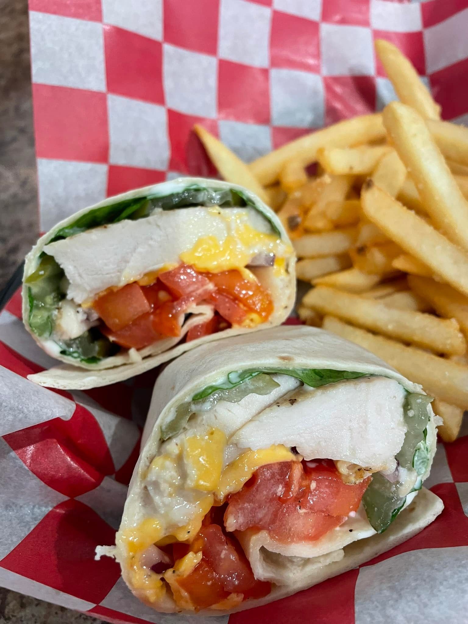 A chicken wrap and french fries on a checkered paper on a table.