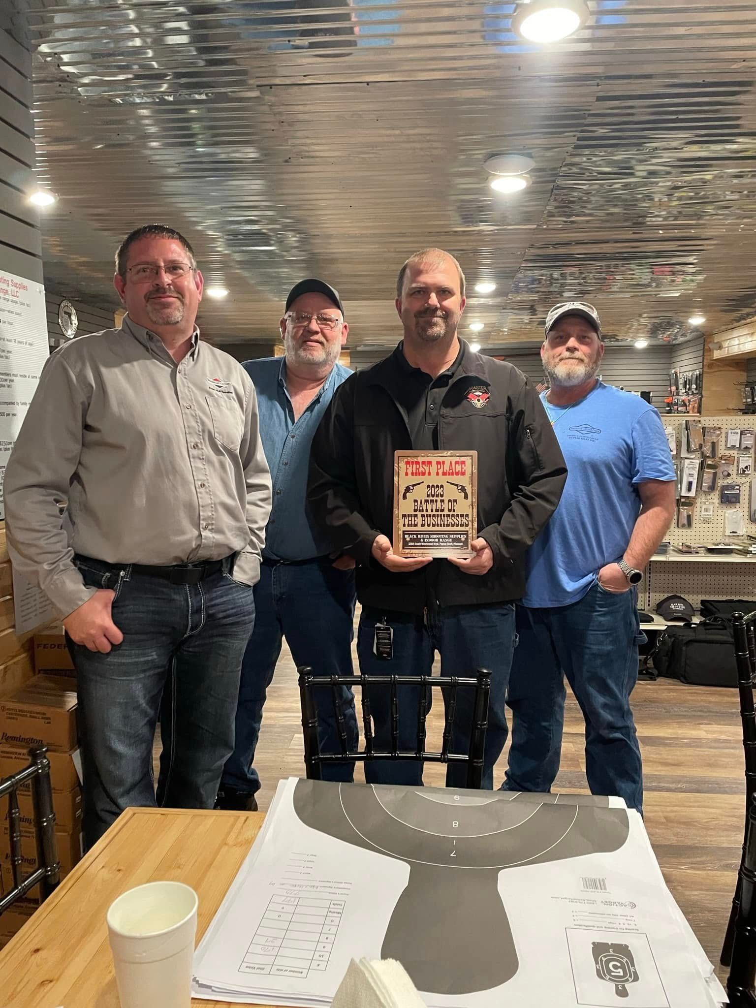A group of men are standing around a table holding a sign.