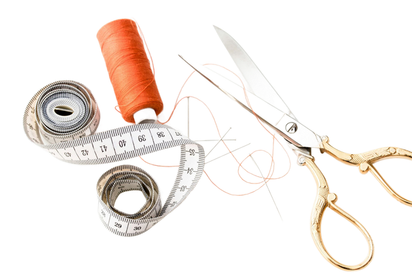 Tape measure, orange thread spool, gold scissors, and thread on white background.