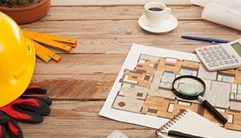 Construction workspace with blueprints, tools, coffee, and a hard hat on a wooden desk.