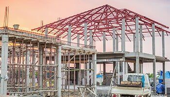 Construction site with concrete frame and red steel roof framework.