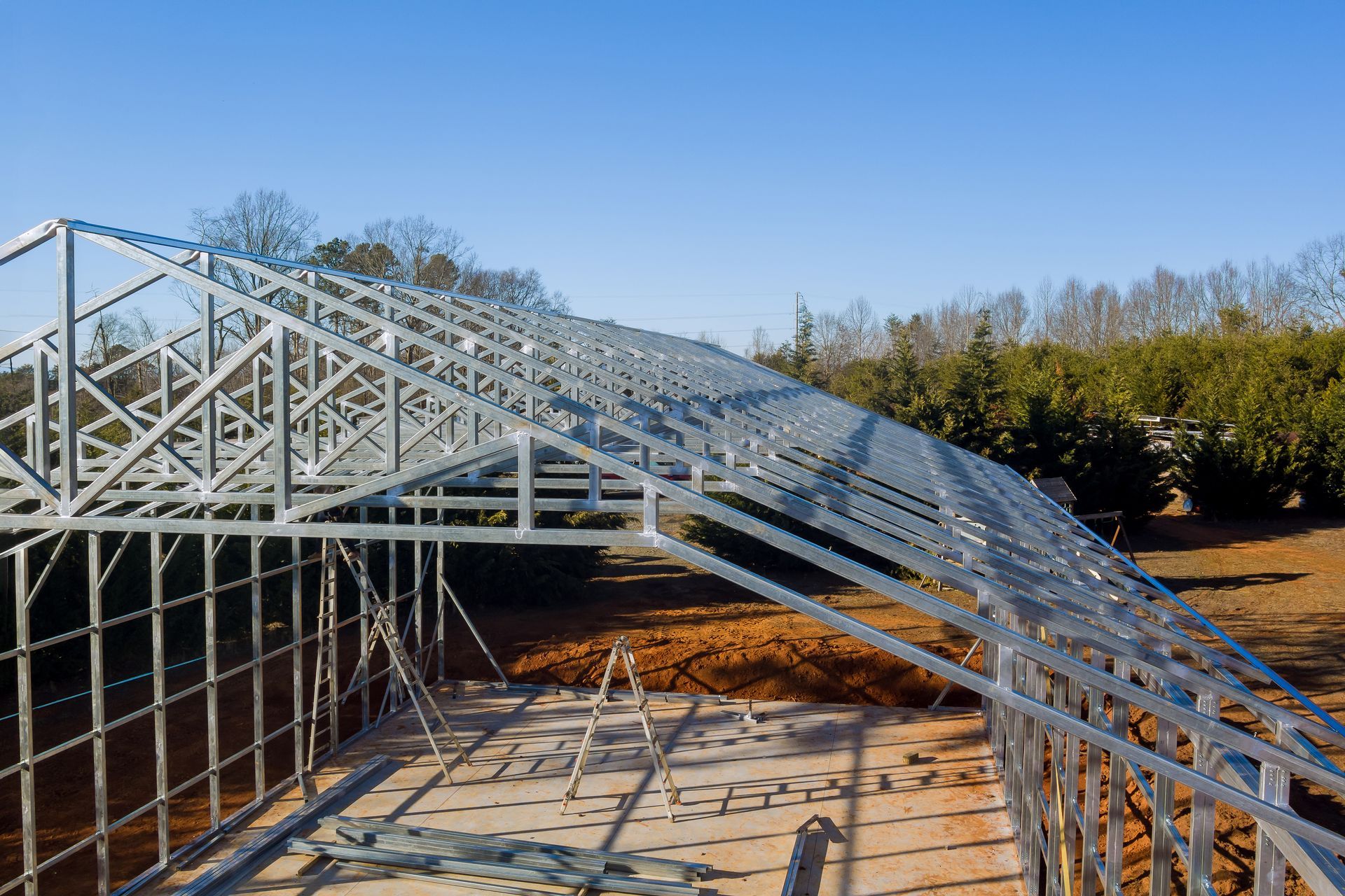 Steel roof framing installed on a building under construction on a clear day.