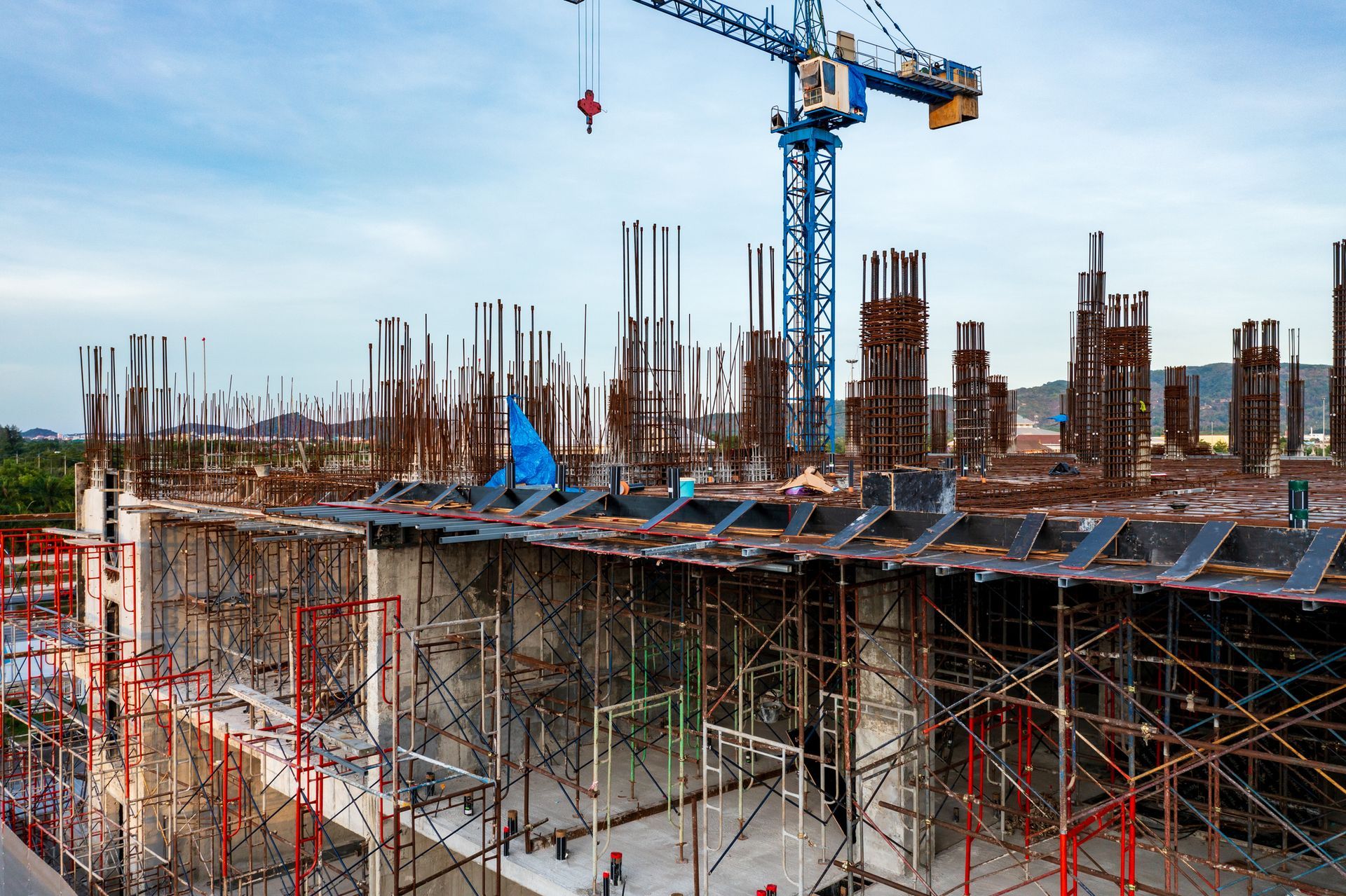 Construction site with a crane towering over reinforced concrete columns, rebar, and scaffolding.