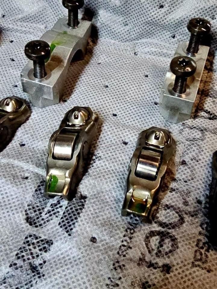 Engine rocker arms and associated mounting hardware on a speckled surface.