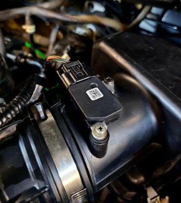 Black sensor mounted on a black air intake box in an engine compartment.
