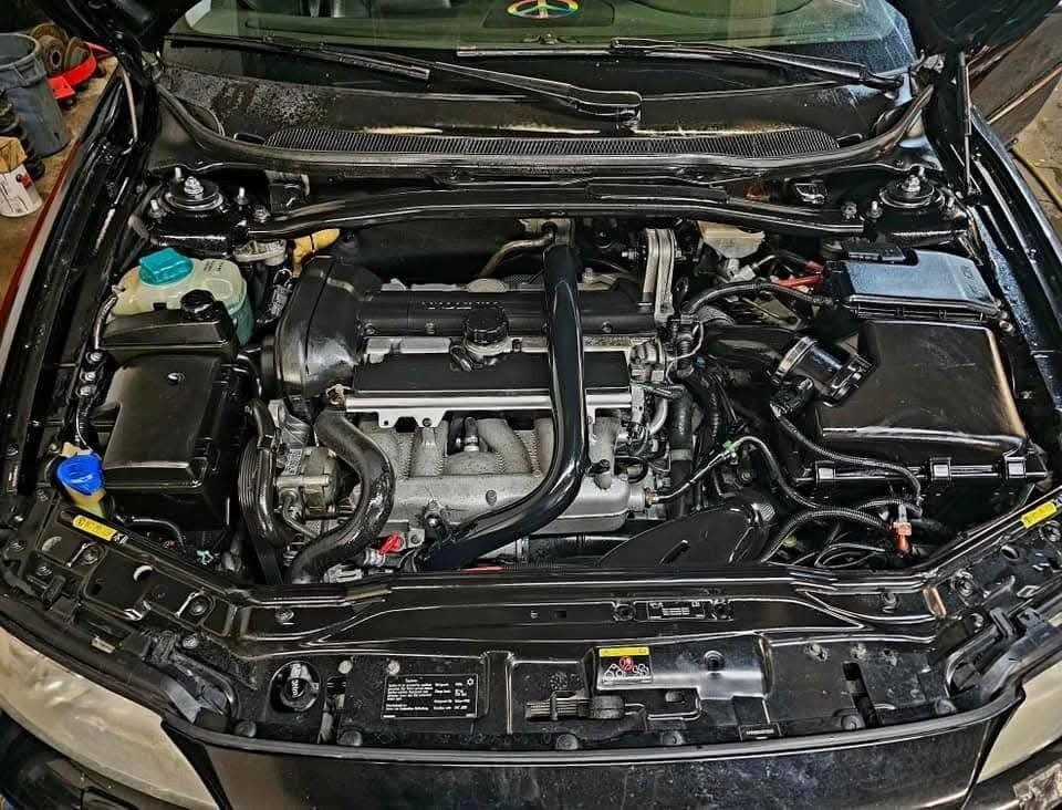 Black car engine bay, open hood.  Engine components, including a coolant reservoir, visible in a dark setting.