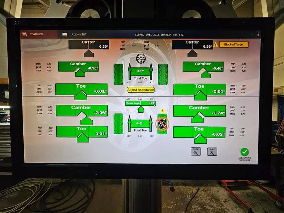 Alignment machine display showing vehicle's camber, toe, and steering angles in green, indicating adjustment status.