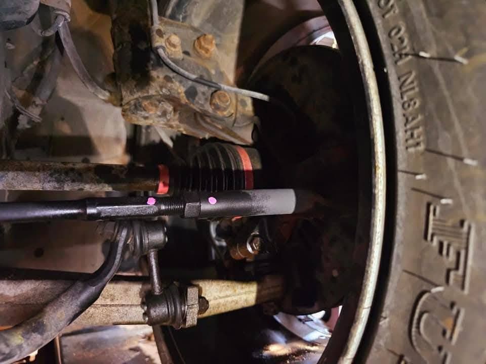 Undercarriage view: Steering linkage near tire and brake rotor, with tie rod and bellows boot.
