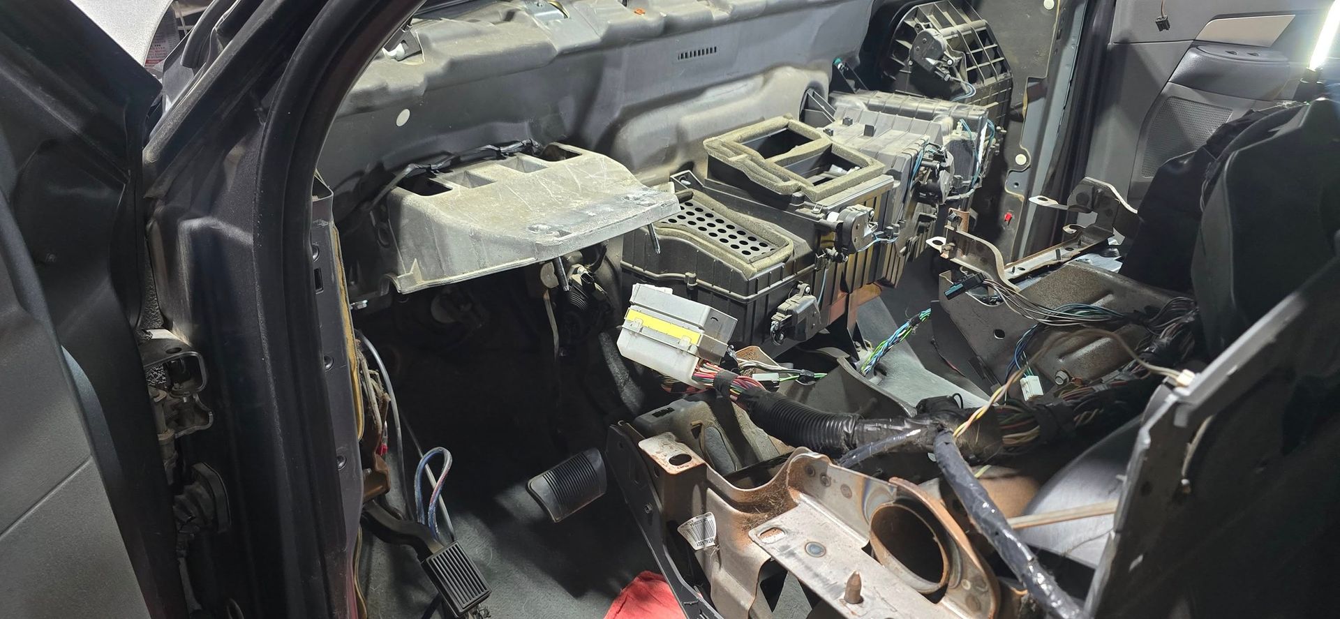 Interior of a car with the dashboard and components disassembled, revealing wires, tubes, and mechanical elements.