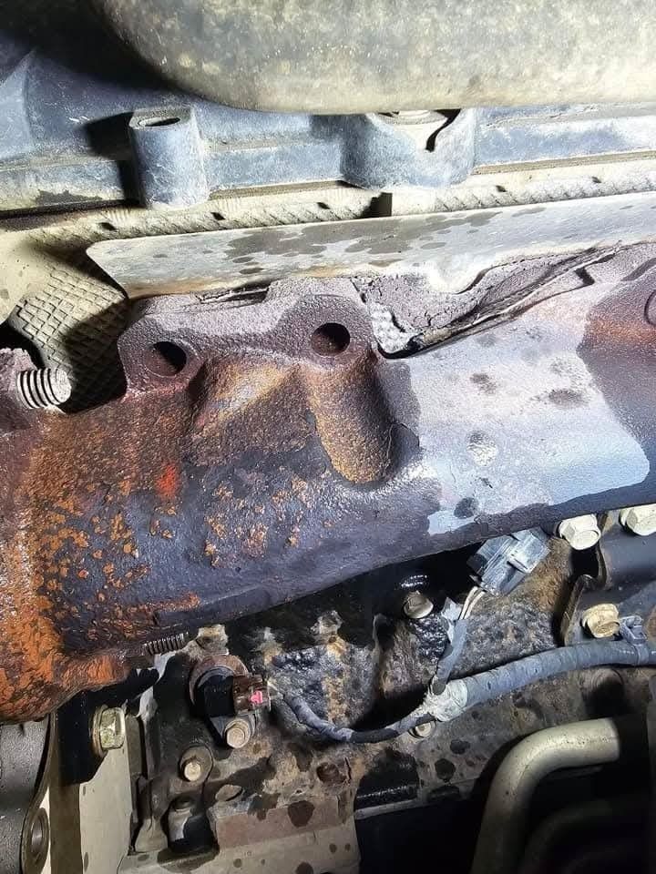 Rusty vehicle exhaust manifold, showing bolt holes and wear.