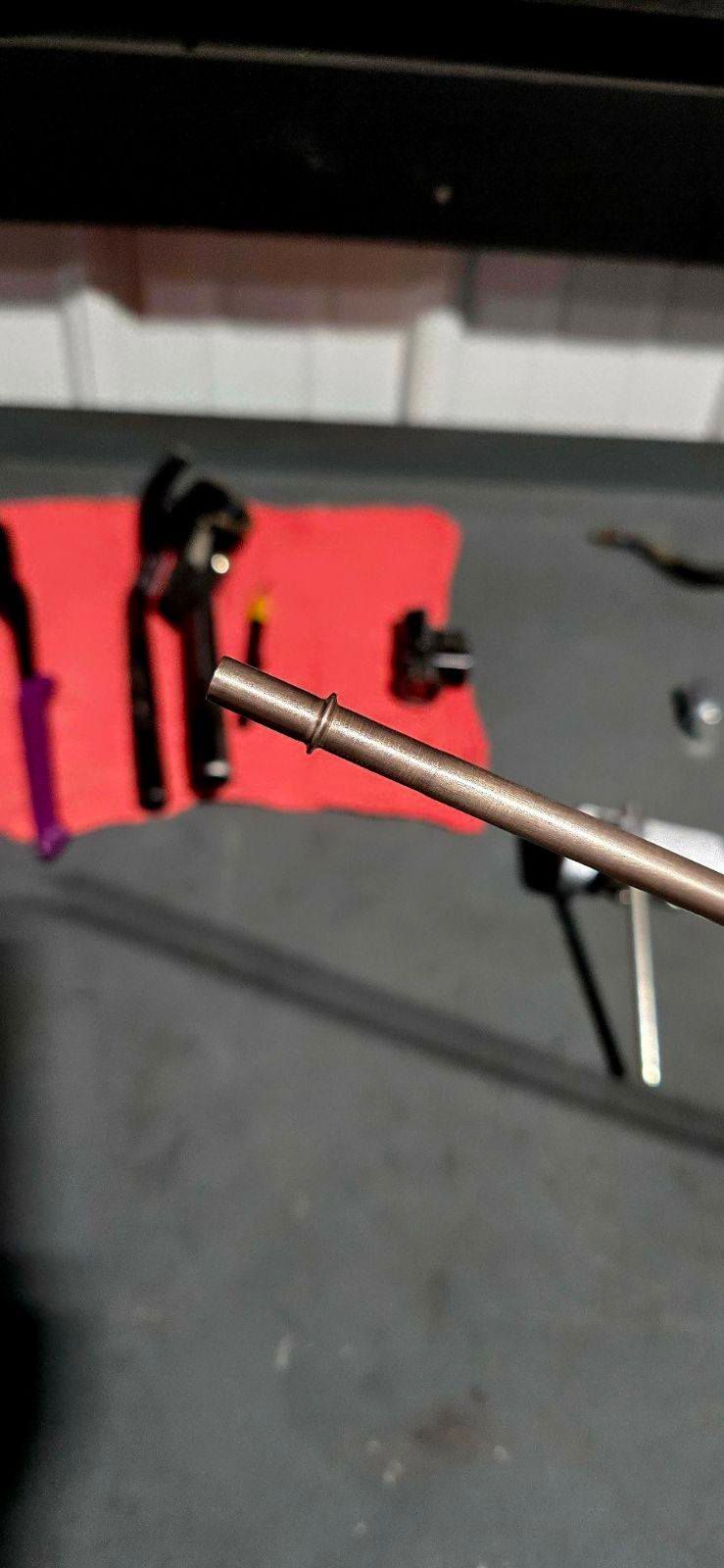 A metal tube with small holes lies on a surface with other tools and a red cloth.