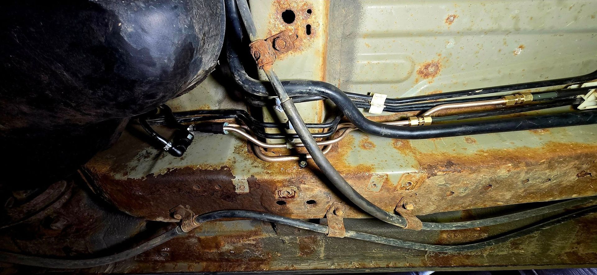 Underside of a car frame with rusted metal, fuel lines, and a black tank.
