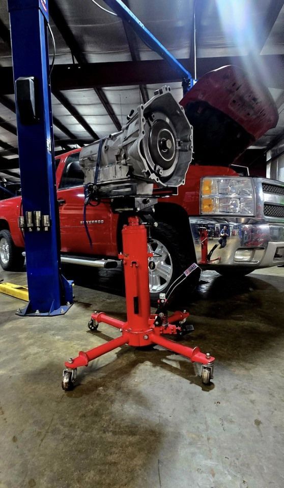 Transmission on a red lift jack in a garage, with a red pickup truck in the background.