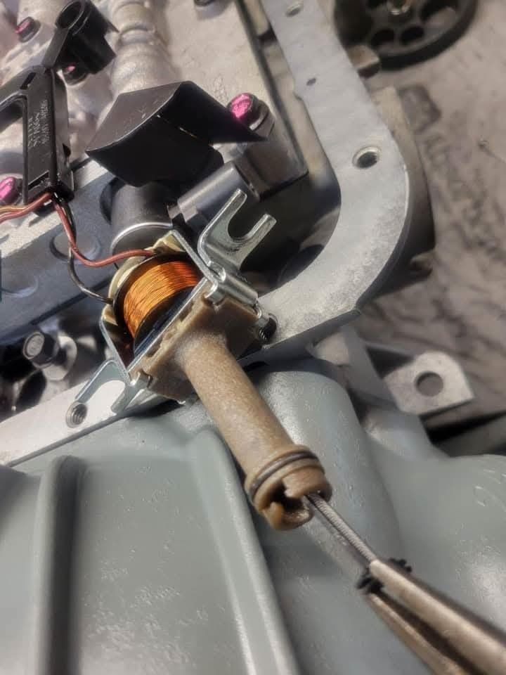 Close-up of a solenoid valve with copper coil, connected to a metal part, in a grey transmission case.