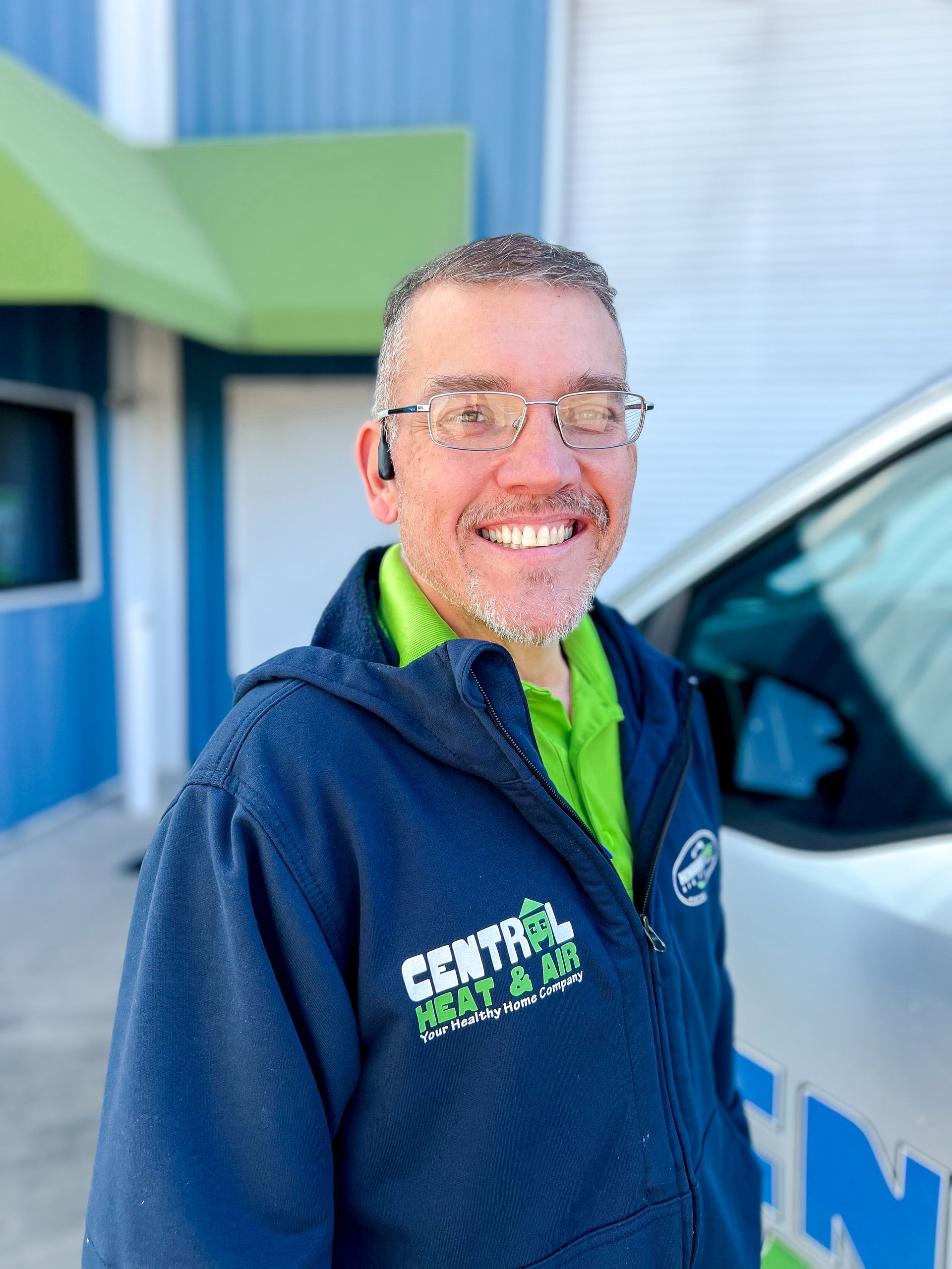 A man in a blue jacket is smiling in front of a brick wall.