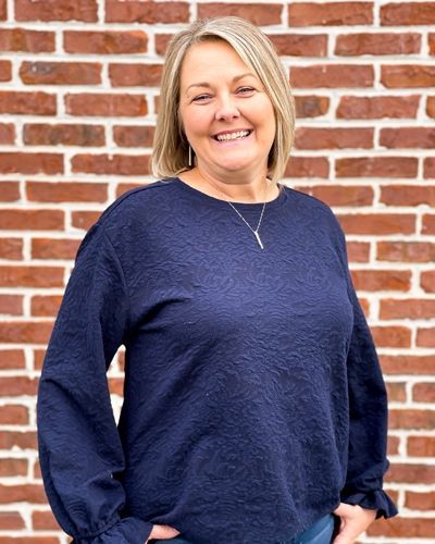 A woman in a blue sweater is standing in front of a brick wall.