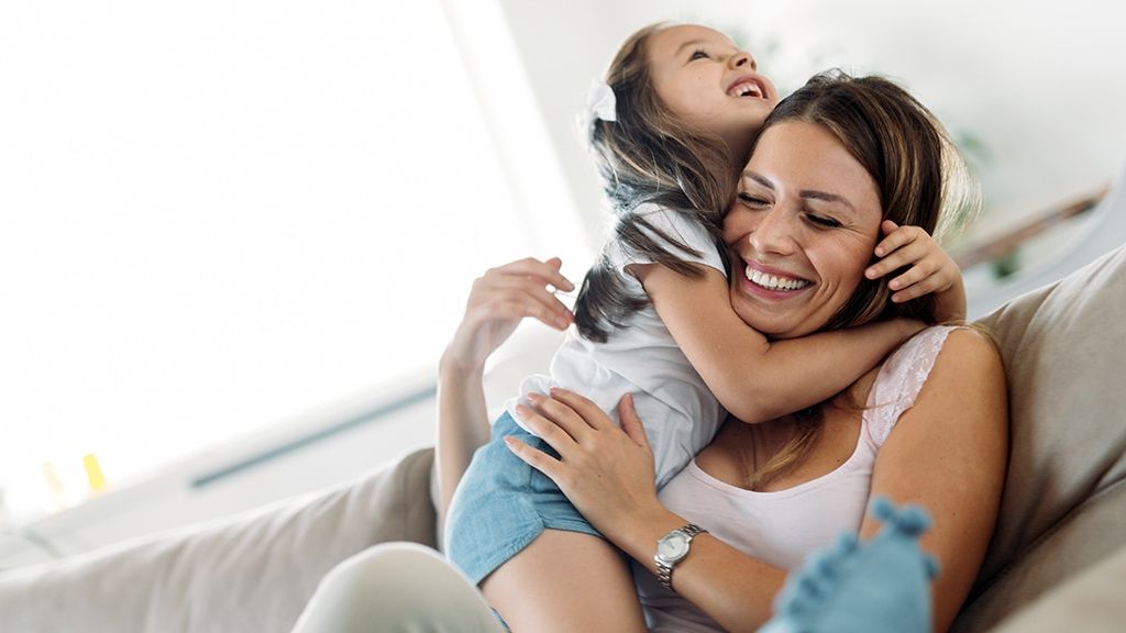 A woman is sitting on a couch holding a little girl in her arms.