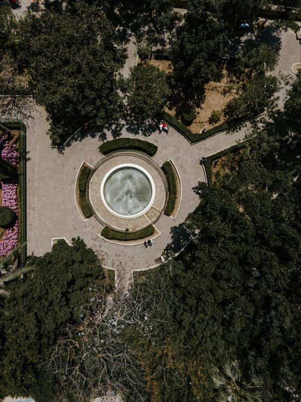 An aerial view of a fountain in a park surrounded by trees.