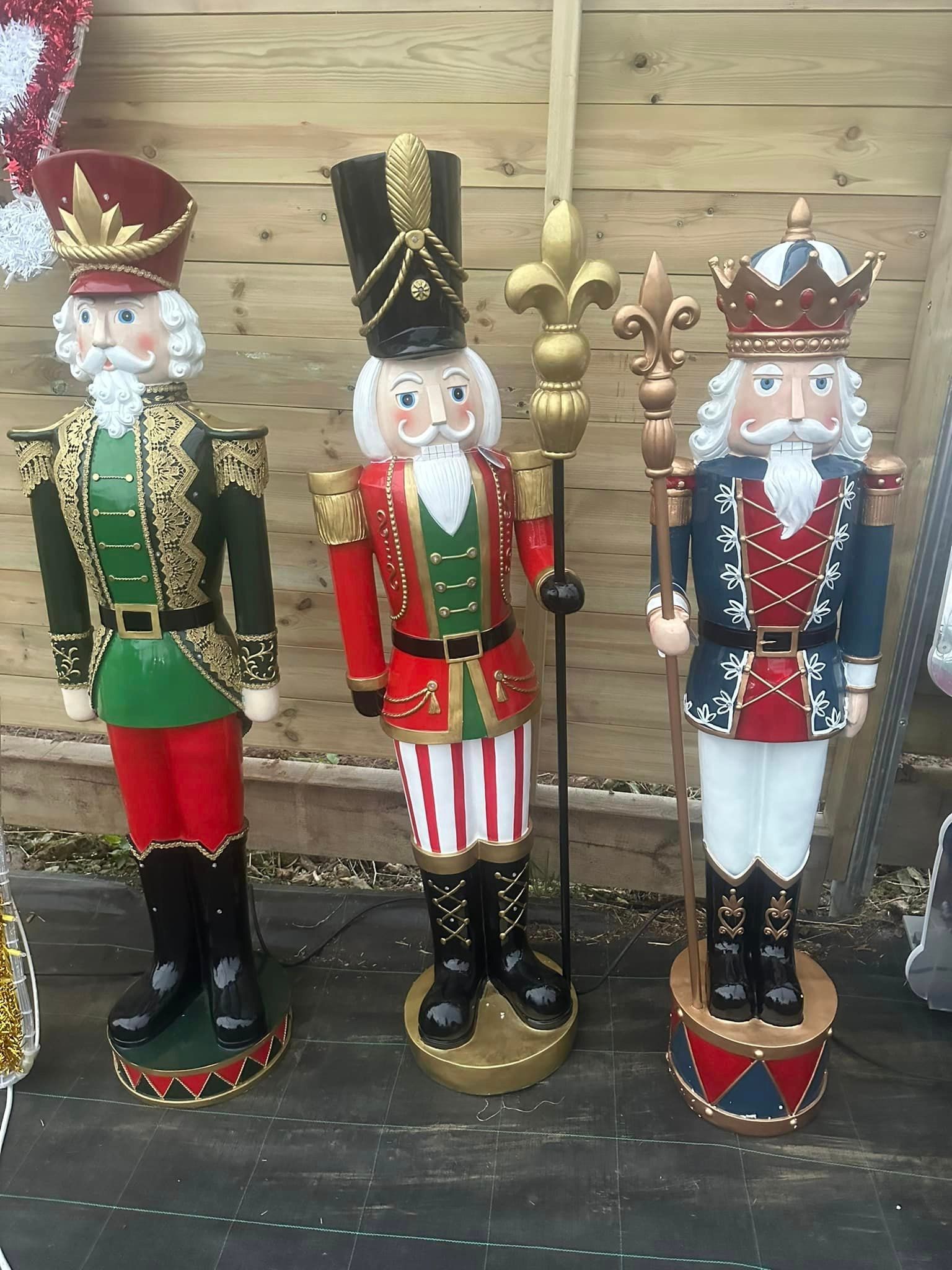 Three festive nutcracker statues: ornate red, green, and blue costumes; holding staffs; against a wooden background.
