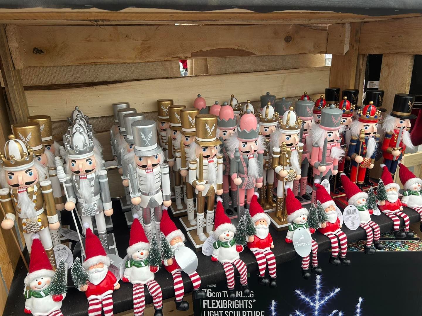 Display of numerous decorative nutcrackers and Santa figures on a shelf, in various colors and styles.