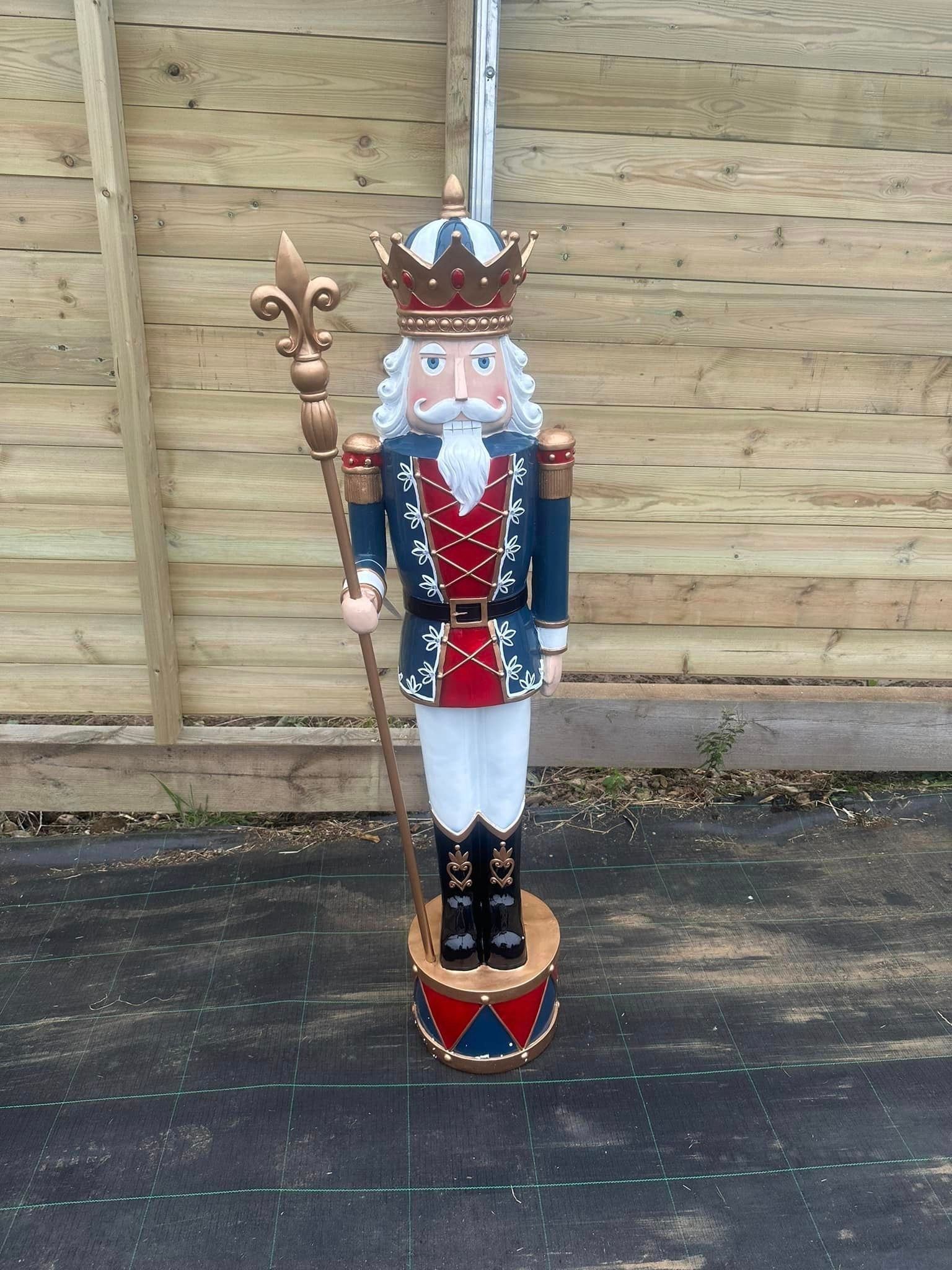 Nutcracker soldier in blue and red uniform, holding staff, atop a drum base.