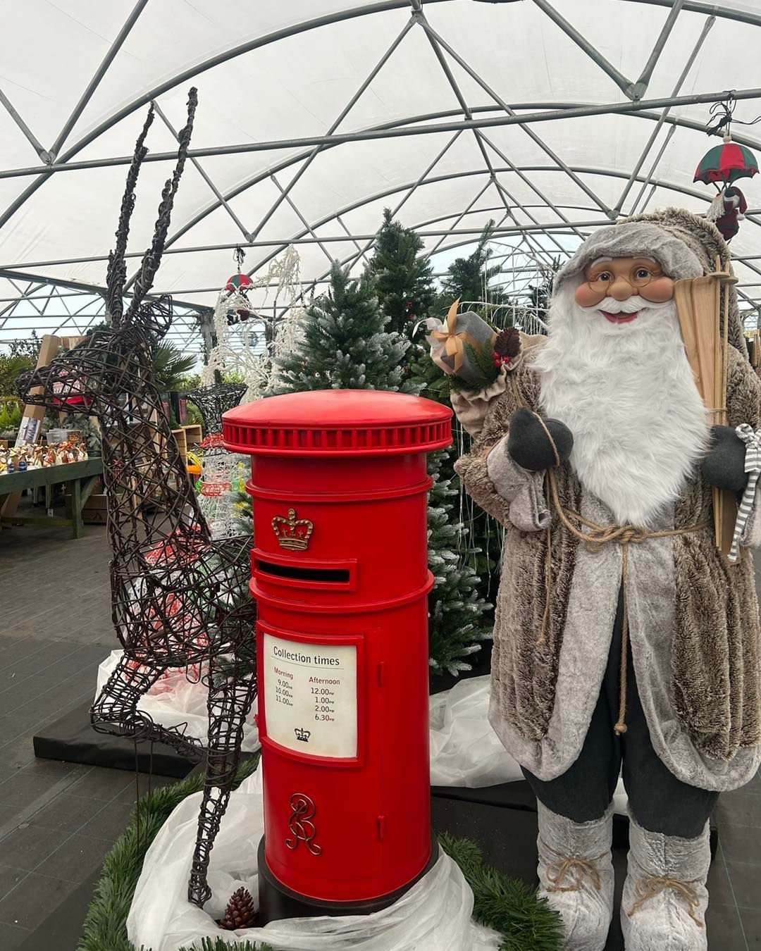 A red British postbox next to Santa Claus decoration with a snowy setting.