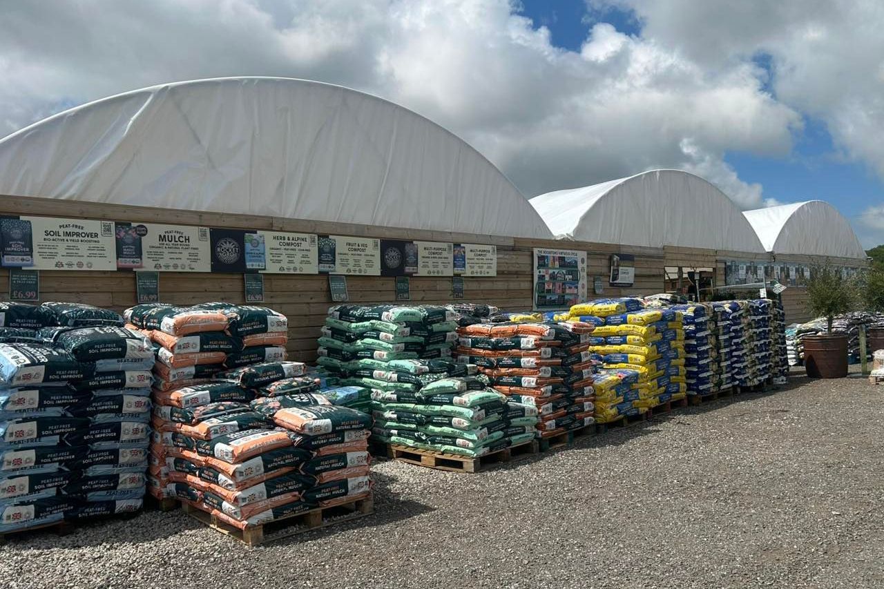 Pallets of bagged products in front of arched, white-roofed buildings on a sunny day.