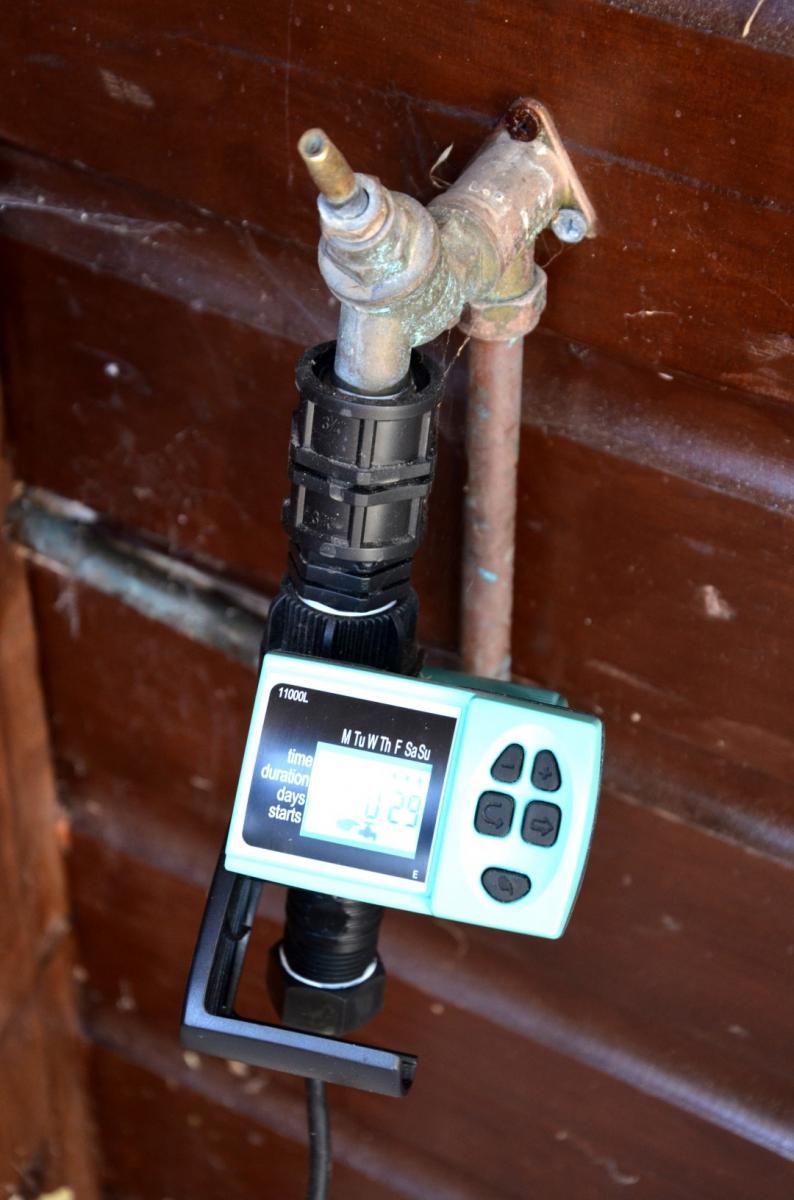 Water faucet with a black timer attached, displaying a digital screen and buttons. Mounted on a brown wooden surface.